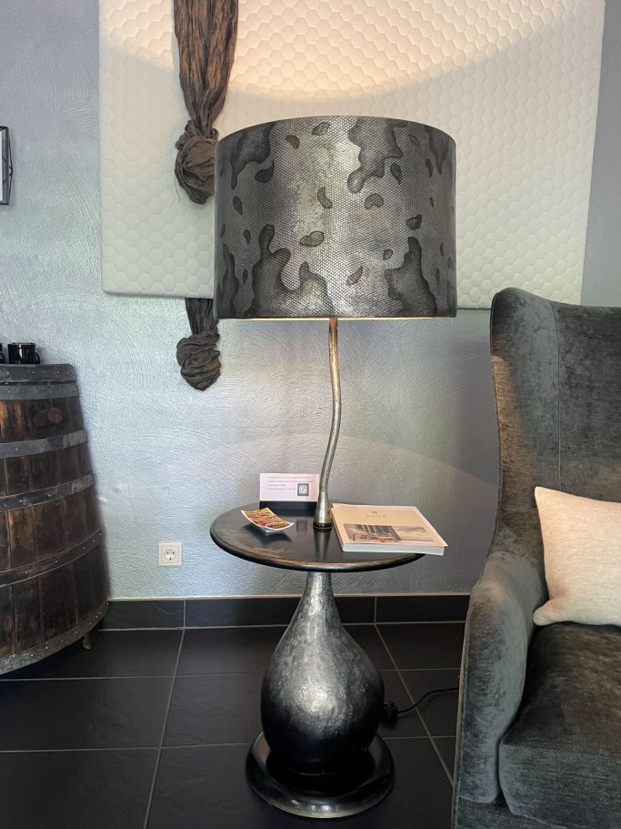Moderne Stehlampe mit dekorativem Lampenschirm neben einem Sessel und Beistelltisch.