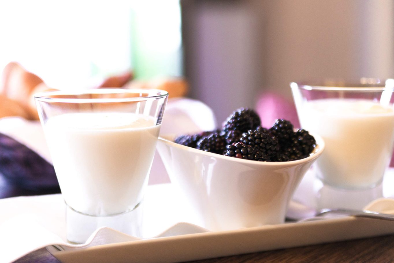 Ein Glas Milch und eine Schale mit schwarzen Früchten auf einem Tisch.