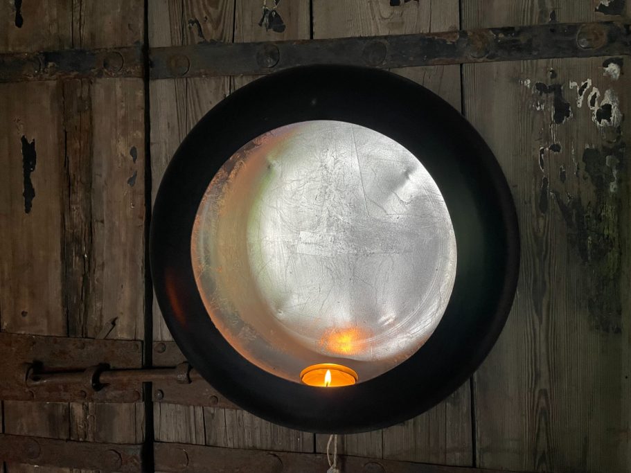 Runder Metallbehälter mit einem schwachen Lichtschein im Inneren, vor einer Holzwand.