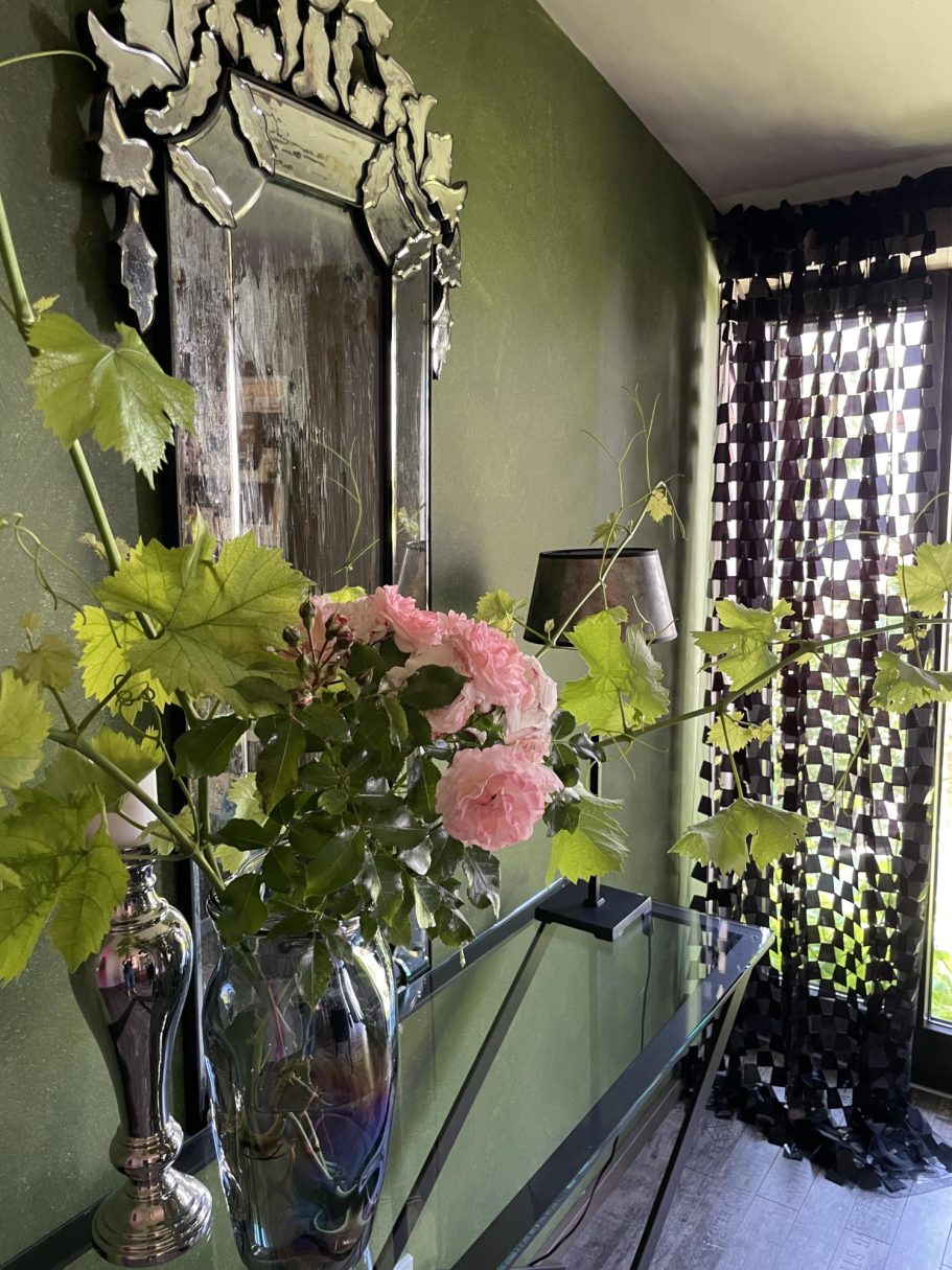 Blumenvase mit rosa Rosen auf einem Tisch vor grünen Wänden und einem Spiegel.