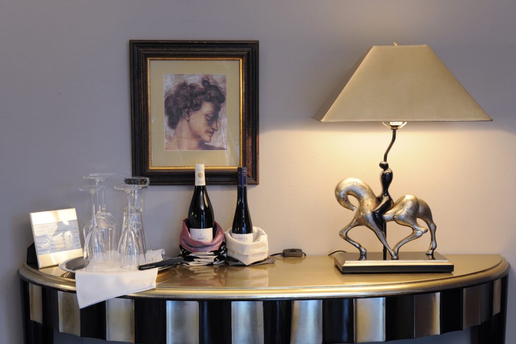 Eleganter Tisch mit zwei Flaschen Wein, Gläsern, einer Lampe und einem dekorativen Pferd.