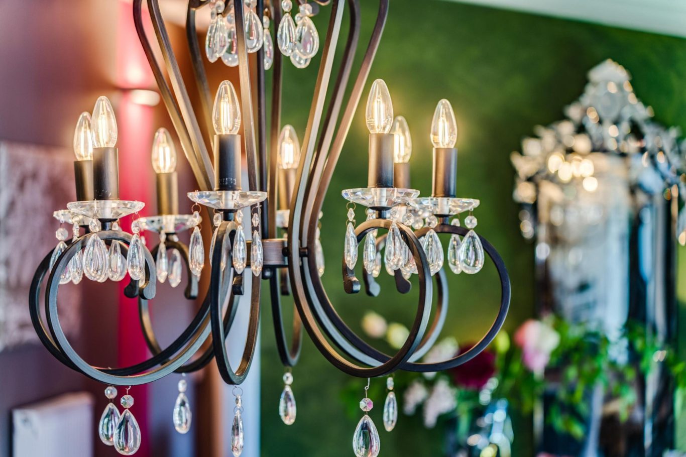 Eleganter Kronleuchter mit Kristallanhängern vor grünem Hintergrund.
