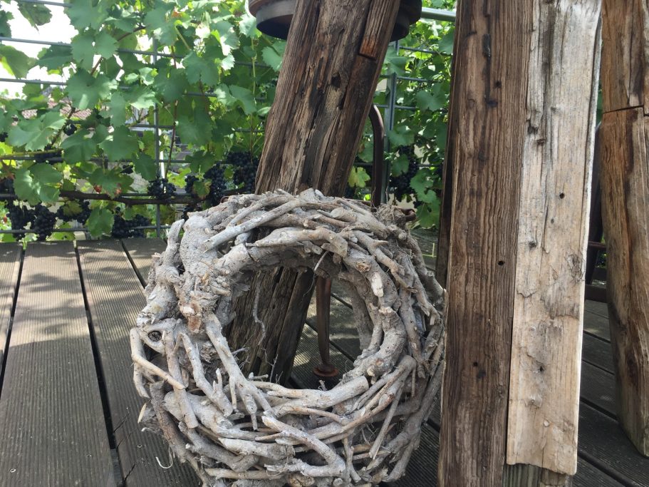 Ein dekorativer Kranz aus Naturmaterialien neben Holzpfosten auf einem Holzboden.