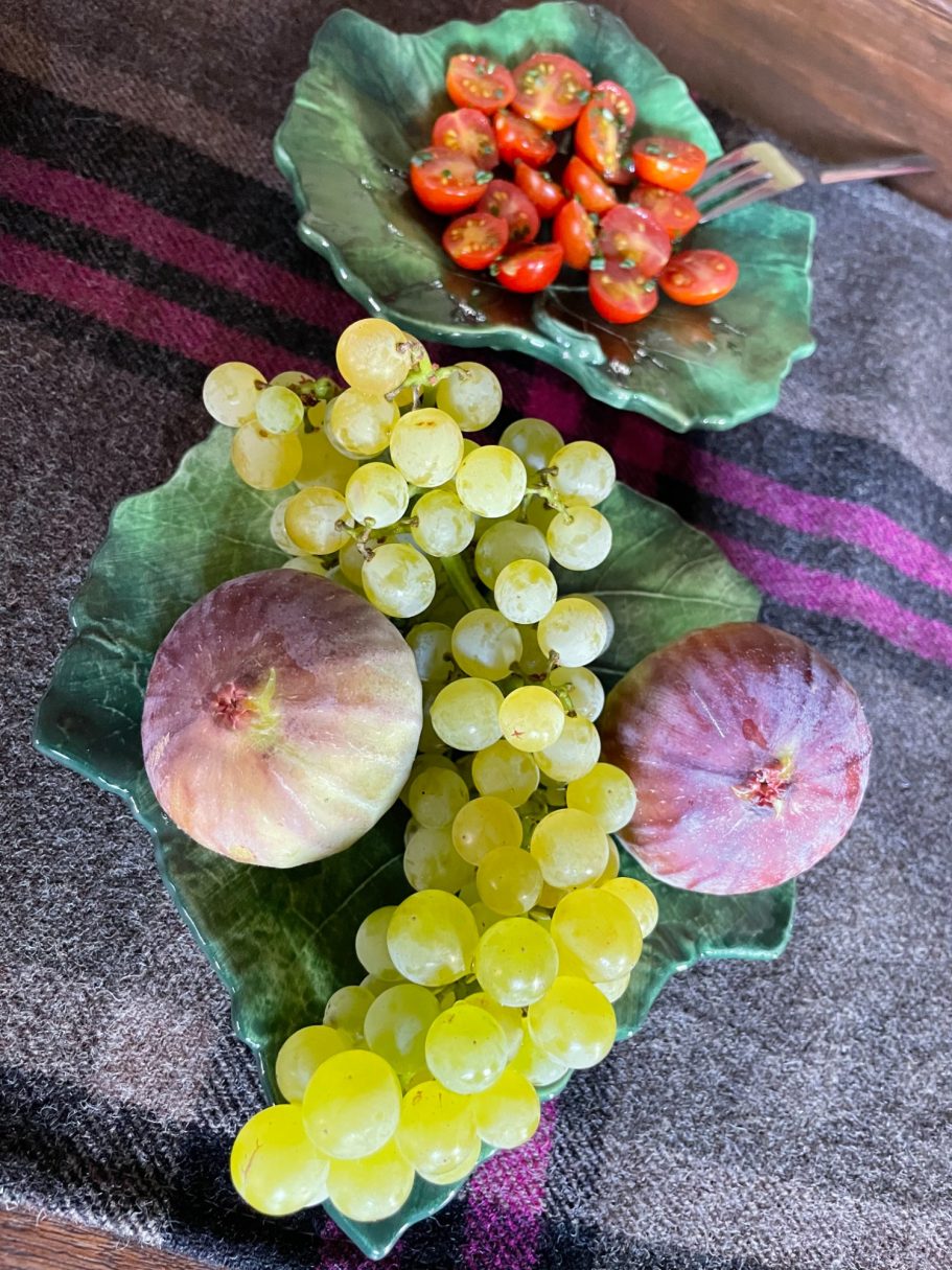 Zwei grüne Trauben, zwei Feigen und eine Schale Kirschtomaten auf einem Tisch.