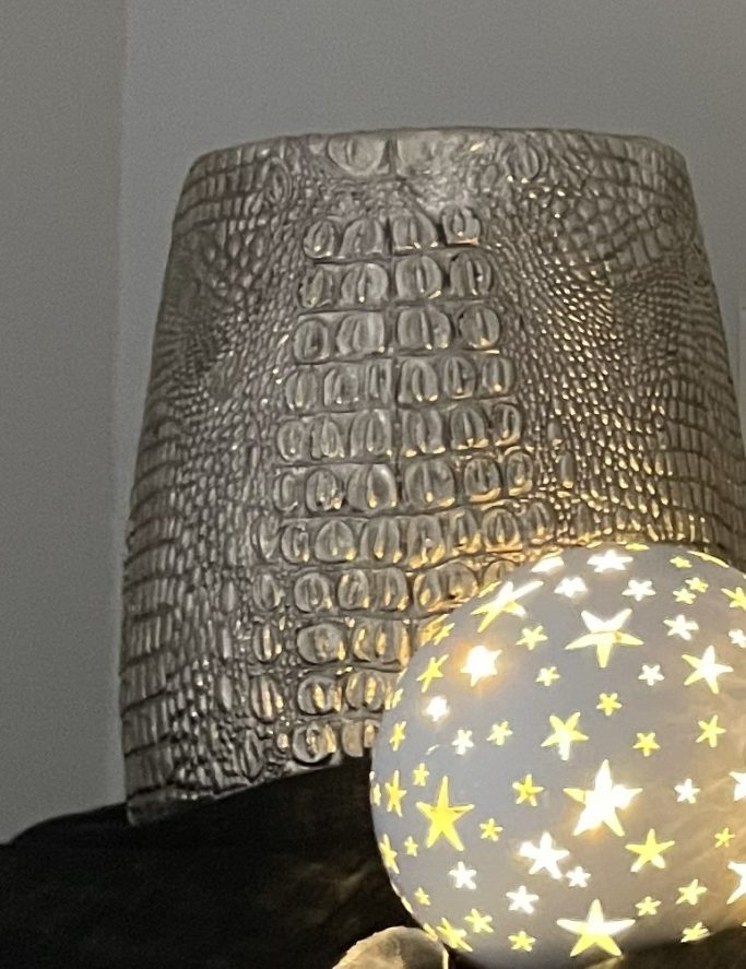 Silberner Lampenschirm mit Krokodilmuster und leuchtender Glaskugel mit Sternen.