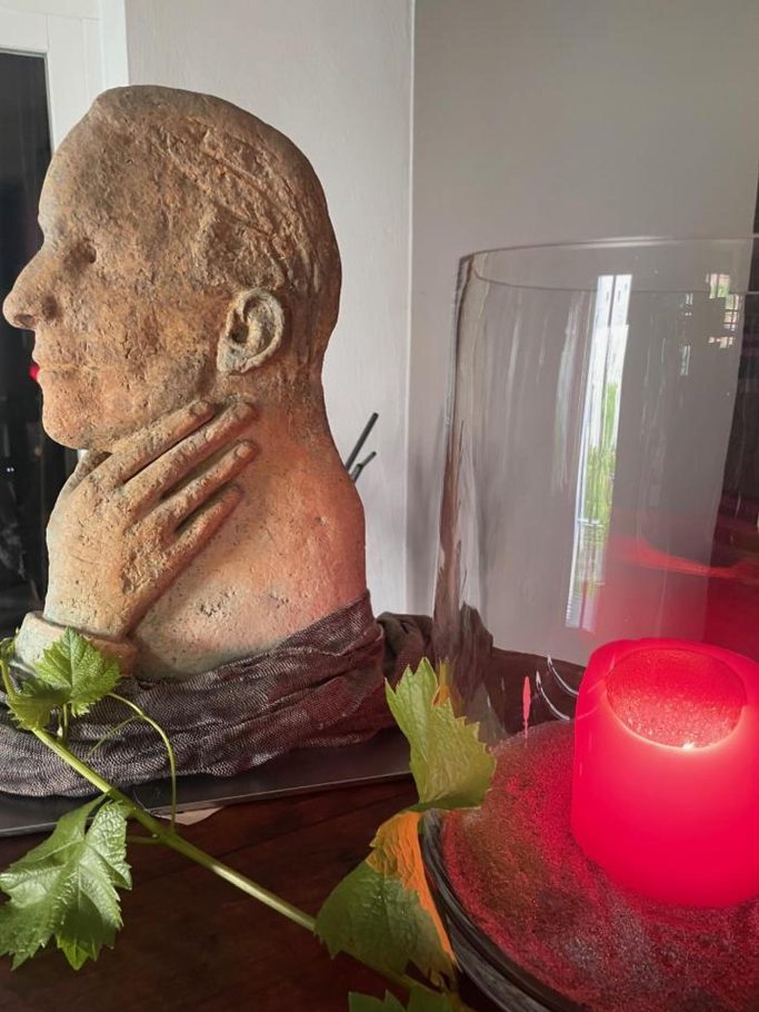 Eine Büste mit angeschlossener Pflanze und einem roten Kerzenlicht im Hintergrund.