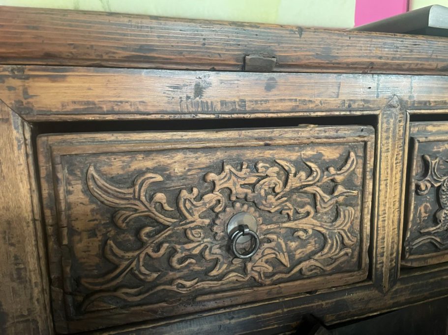 Detail eines kunstvoll geschnitzten Holzschranks mit floralen Mustern.