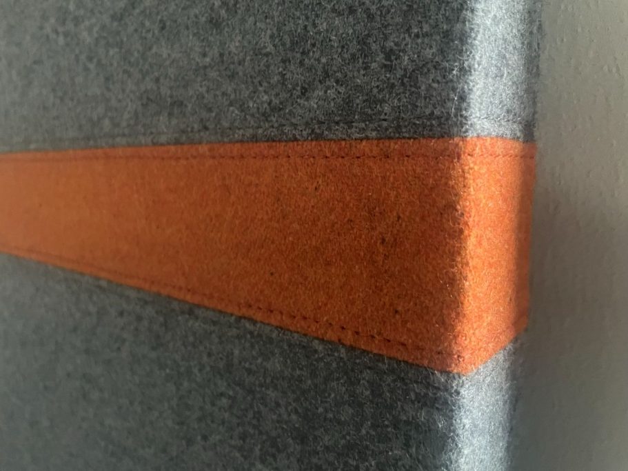 Grau gefilztes Material mit einer orangefarbenen Naht.