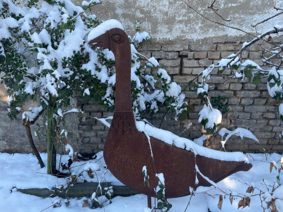 Eine braune, schneebedeckte Skulptur eines Vogels steht in einem winterlichen Garten.